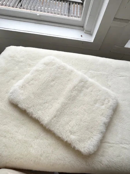 Two white fluffy bath mats on a light-colored floor with a window in the background.